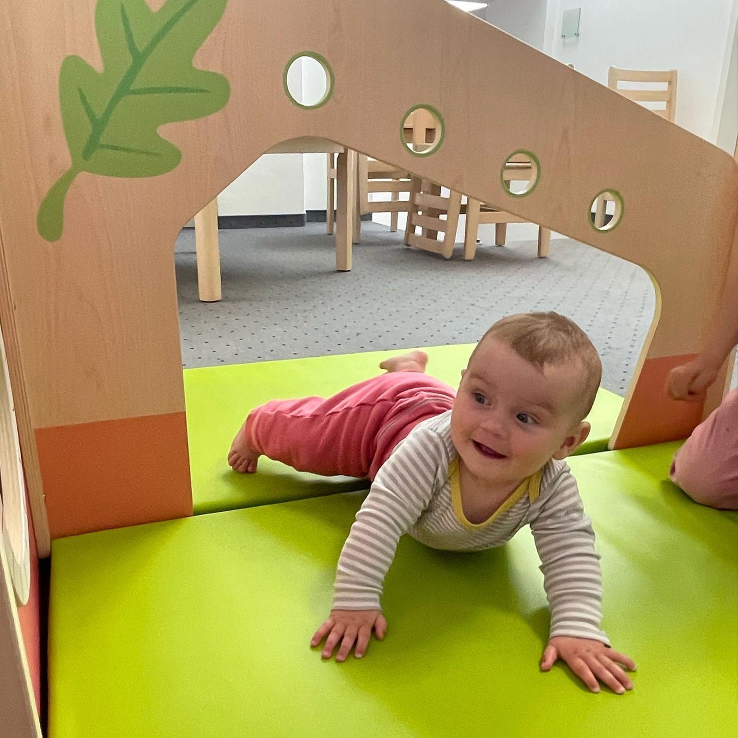 Baby crawling on a green mat inside a wooden play structure.