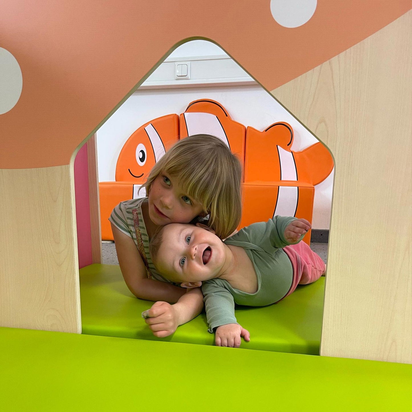 Two children playing inside a colorful playhouse with a clownfish design in the background.